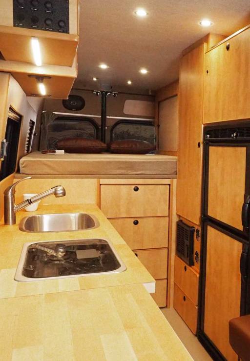 Sprinter interior with maple cabinets and a refrigerator.