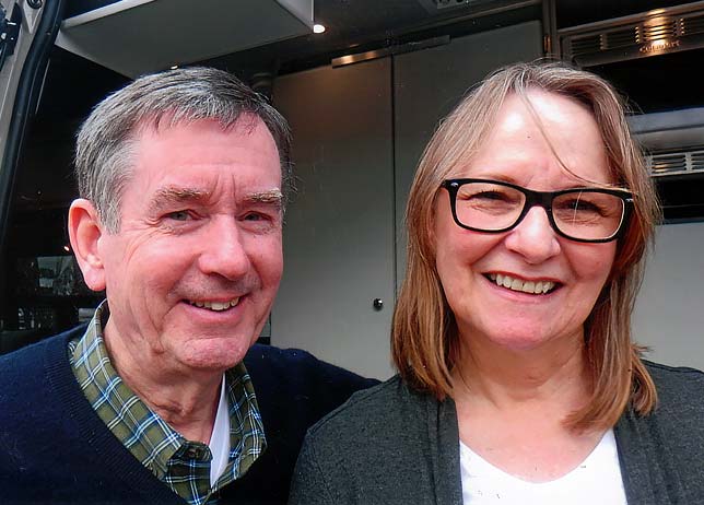 The Harrisons smiling next to their grey custom Sportsmobile camper van conversion.